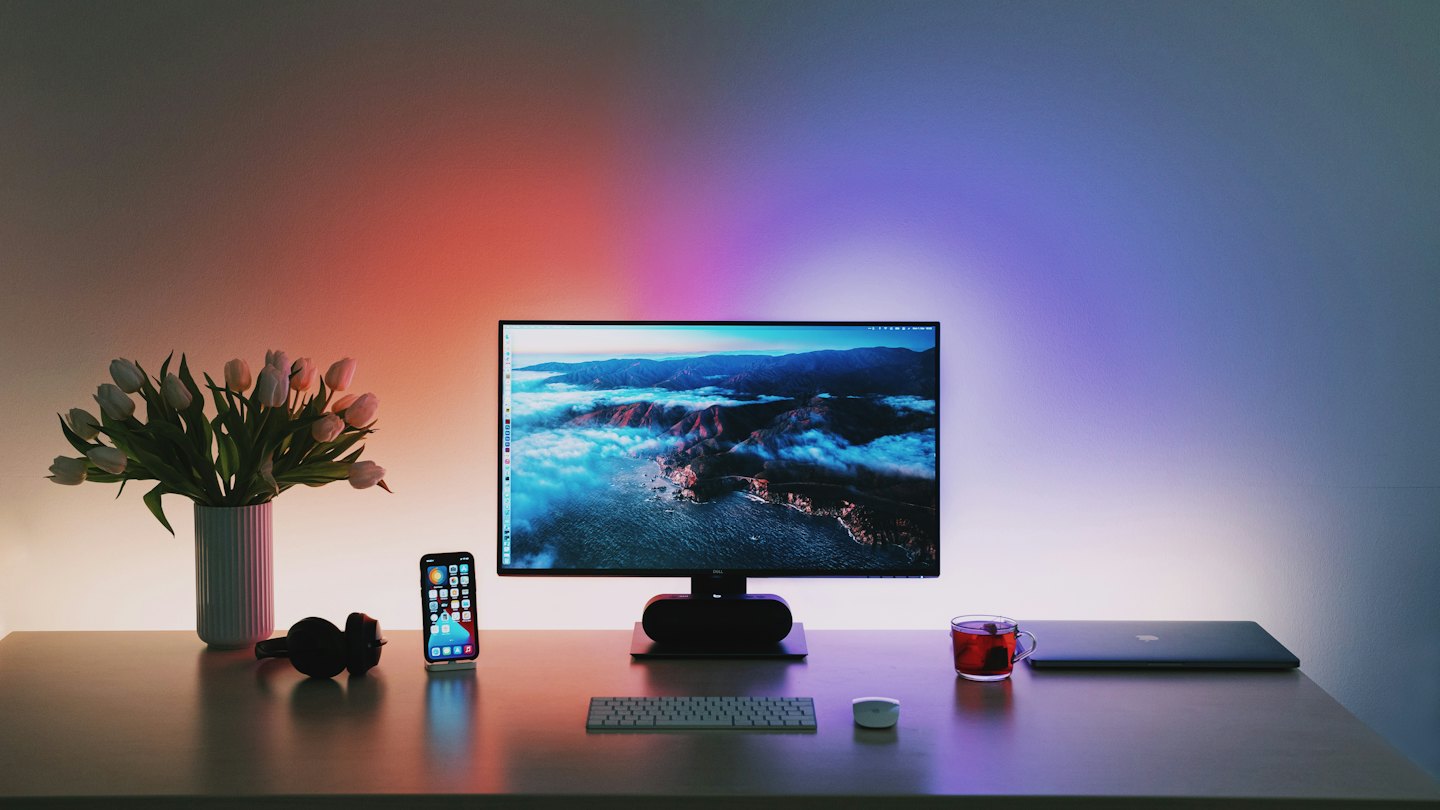 A modern office desk with a computer displaying a cloudscape and white tulips.